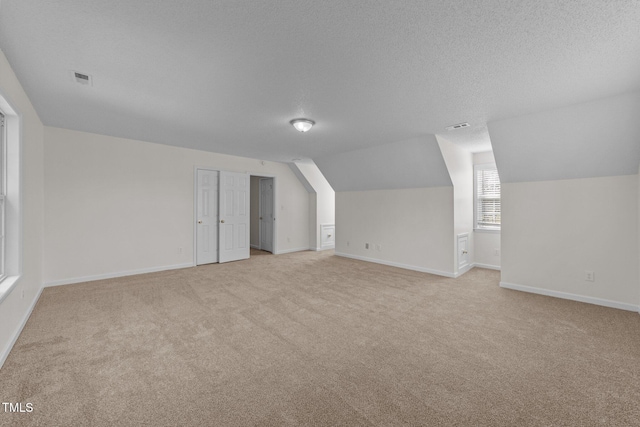 additional living space with visible vents, light carpet, vaulted ceiling, a textured ceiling, and baseboards