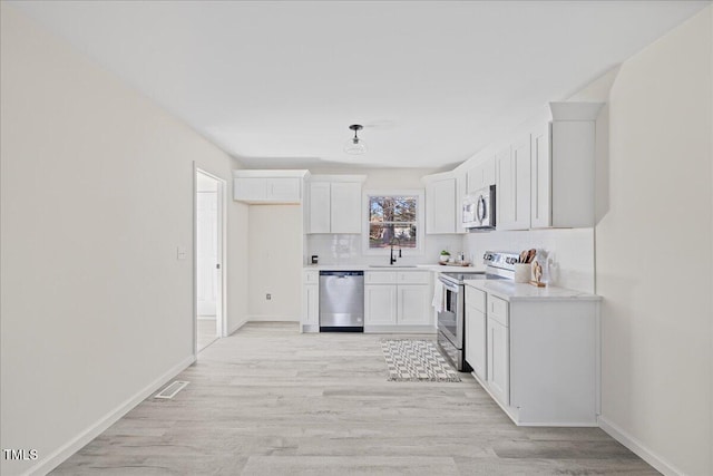 kitchen with white cabinets, decorative backsplash, light wood-type flooring, and appliances with stainless steel finishes