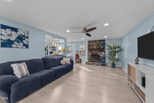 living room featuring ceiling fan, light wood-type flooring, and a stone fireplace