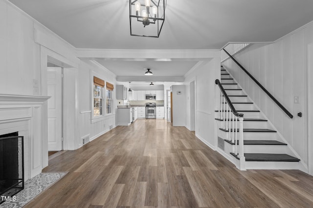 unfurnished living room with crown molding, sink, wood-type flooring, and a notable chandelier