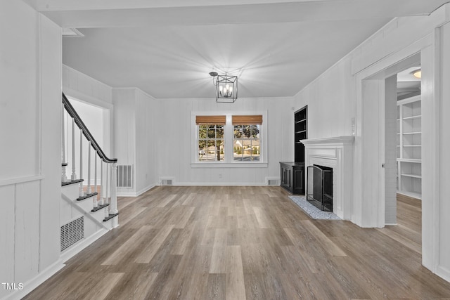 unfurnished living room featuring built in shelves, light hardwood / wood-style flooring, and a notable chandelier