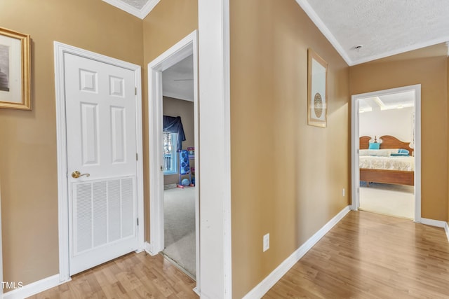 corridor featuring a textured ceiling, light hardwood / wood-style flooring, and crown molding