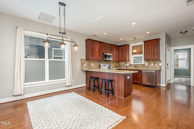 kitchen with sink, hanging light fixtures, kitchen peninsula, a breakfast bar, and appliances with stainless steel finishes