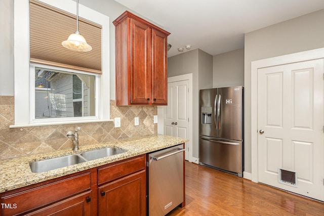 kitchen featuring tasteful backsplash, light stone counters, stainless steel appliances, sink, and decorative light fixtures