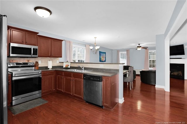 kitchen featuring dark hardwood / wood-style flooring, backsplash, ceiling fan with notable chandelier, stainless steel appliances, and hanging light fixtures