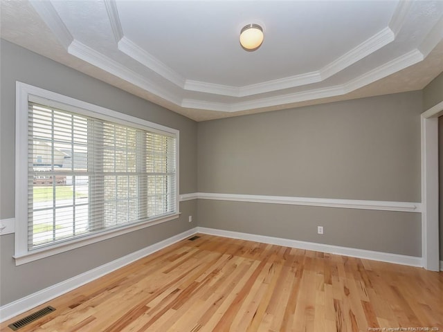 unfurnished room with hardwood / wood-style floors, a raised ceiling, and ornamental molding