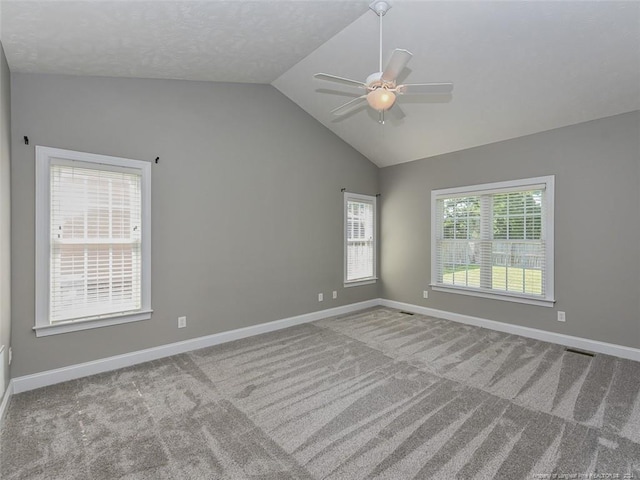 carpeted empty room featuring ceiling fan, lofted ceiling, and a wealth of natural light