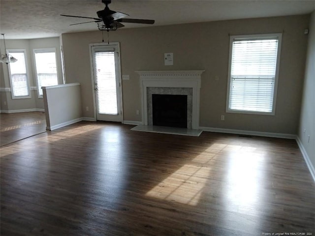 unfurnished living room with ceiling fan with notable chandelier, dark hardwood / wood-style floors, and a wealth of natural light