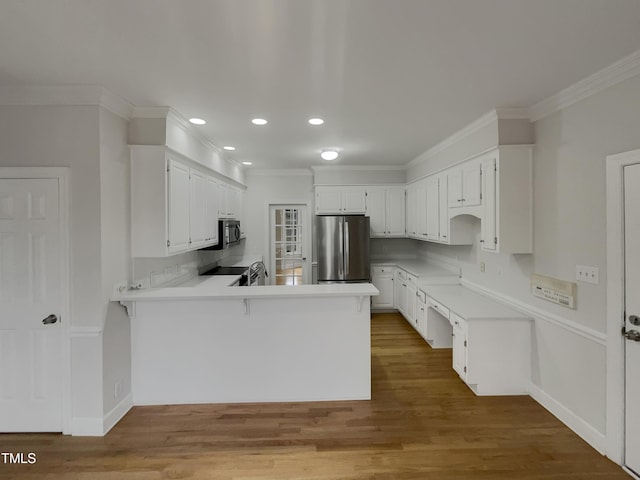 kitchen featuring backsplash, white cabinets, hardwood / wood-style flooring, kitchen peninsula, and stainless steel appliances