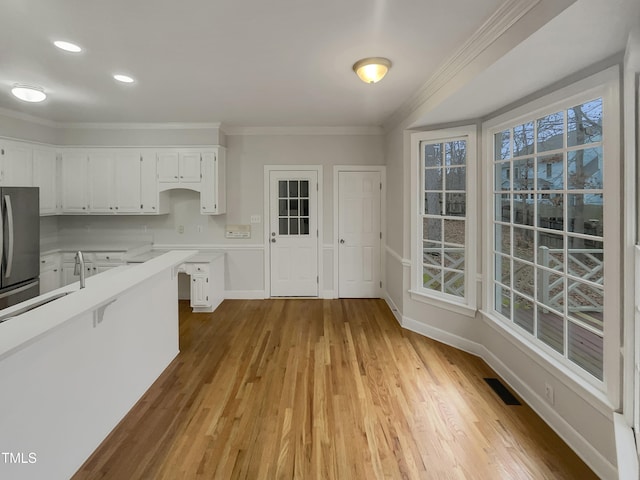 kitchen with stainless steel refrigerator, white cabinetry, plenty of natural light, light hardwood / wood-style floors, and ornamental molding