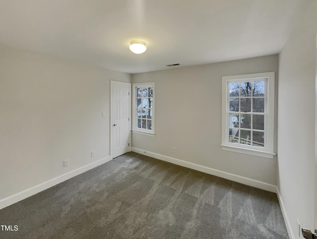 spare room with dark colored carpet and plenty of natural light