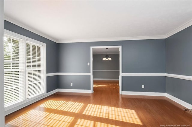 spare room featuring wood-type flooring, ornamental molding, and an inviting chandelier