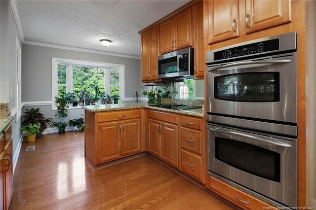 kitchen with light stone countertops, appliances with stainless steel finishes, kitchen peninsula, and ornamental molding