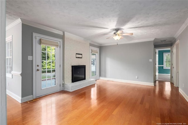 unfurnished living room featuring ceiling fan, crown molding, wood-type flooring, a textured ceiling, and a fireplace