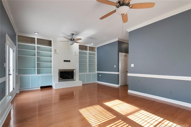 unfurnished living room featuring built in shelves, crown molding, hardwood / wood-style floors, and ceiling fan