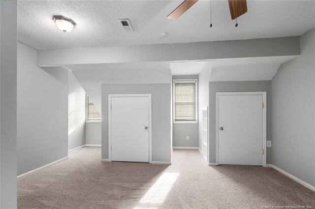 additional living space featuring ceiling fan, light colored carpet, and a textured ceiling