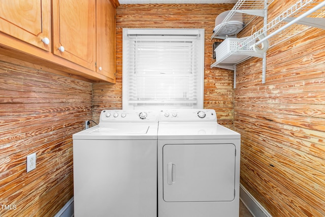 clothes washing area featuring wooden walls, washer and dryer, and cabinets