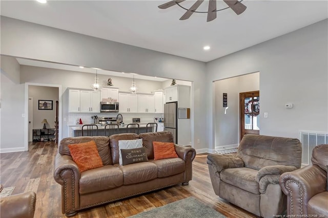 living room featuring baseboards, visible vents, a ceiling fan, wood finished floors, and recessed lighting