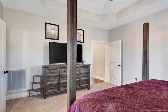 bedroom with a tray ceiling, visible vents, light carpet, and baseboards