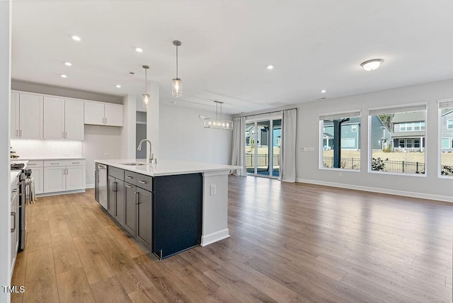 kitchen featuring white cabinets, decorative light fixtures, sink, and a center island with sink