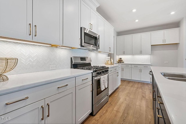 kitchen with stainless steel appliances, light hardwood / wood-style floors, decorative backsplash, white cabinets, and sink