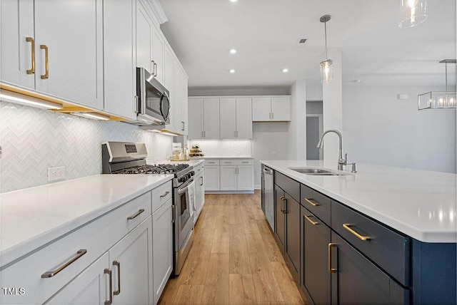 kitchen with a center island with sink, appliances with stainless steel finishes, pendant lighting, sink, and white cabinetry