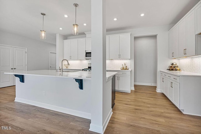 kitchen featuring a kitchen island with sink, hanging light fixtures, light wood-type flooring, sink, and white cabinetry