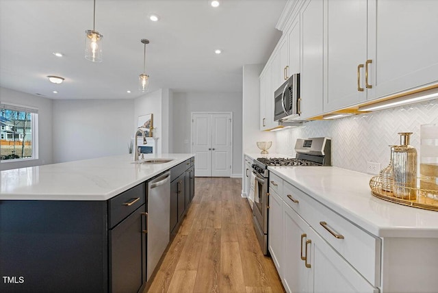 kitchen with a kitchen island with sink, appliances with stainless steel finishes, hanging light fixtures, sink, and white cabinetry