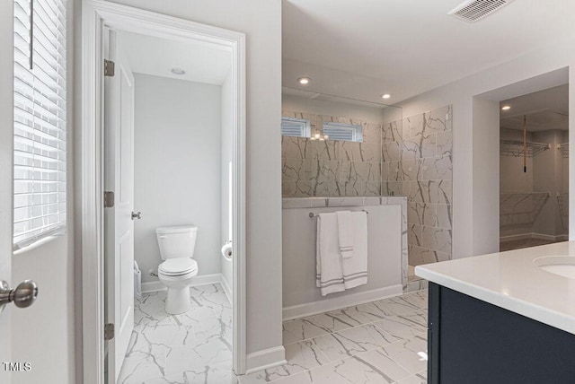 bathroom with toilet, a tile shower, and vanity