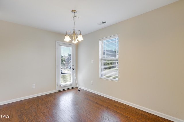 empty room with dark wood-type flooring and a notable chandelier