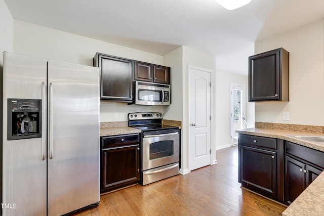 kitchen with appliances with stainless steel finishes, dark brown cabinetry, light hardwood / wood-style floors, and sink