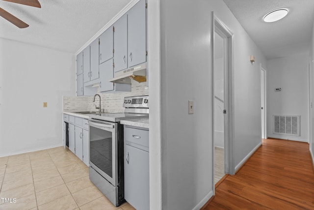 kitchen featuring tasteful backsplash, ceiling fan, sink, light tile patterned floors, and stainless steel electric range