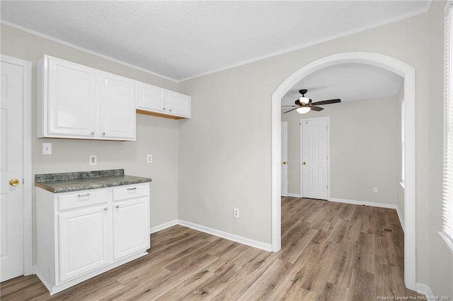 kitchen with ceiling fan, white cabinets, ornamental molding, and light wood-type flooring