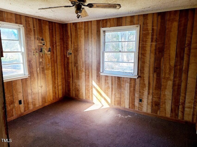 unfurnished room with a textured ceiling, ceiling fan, and wooden walls