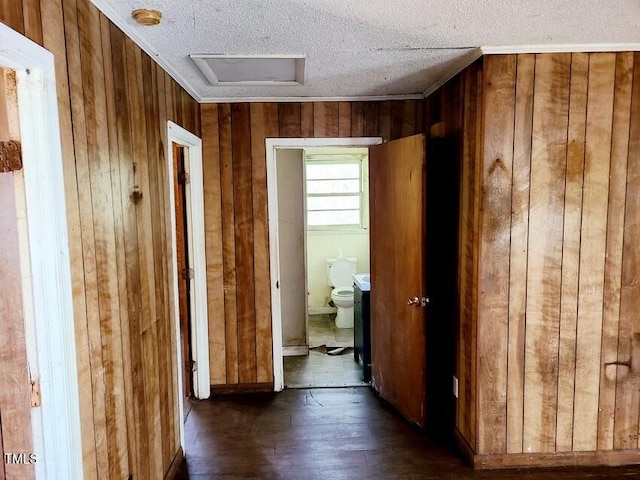 hall featuring a textured ceiling, dark hardwood / wood-style floors, crown molding, and wooden walls