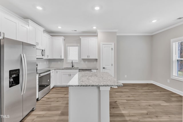 kitchen with light stone countertops, a kitchen island, appliances with stainless steel finishes, white cabinets, and ornamental molding