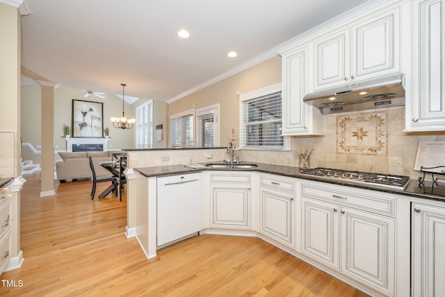 kitchen with stainless steel gas stovetop, dark stone counters, white dishwasher, sink, and kitchen peninsula