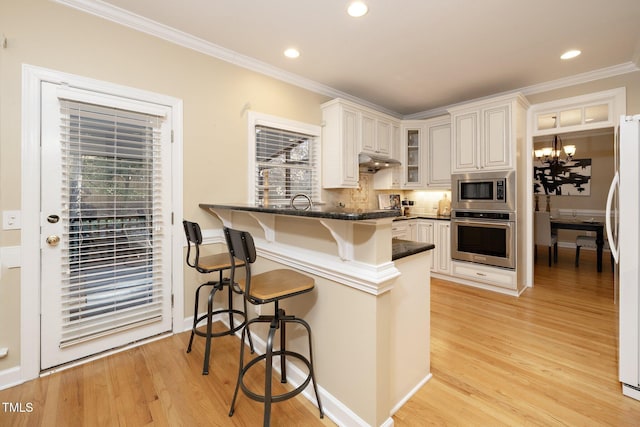 kitchen with kitchen peninsula, stainless steel appliances, an inviting chandelier, white cabinetry, and a breakfast bar area