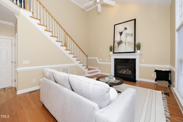 living room featuring hardwood / wood-style floors, ceiling fan, crown molding, and a tiled fireplace