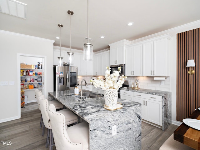 kitchen featuring white cabinets, appliances with stainless steel finishes, a center island with sink, and hanging light fixtures