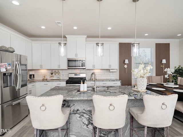 kitchen with white cabinets, an island with sink, pendant lighting, and appliances with stainless steel finishes