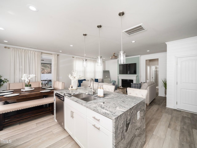 kitchen featuring light stone counters, a kitchen island with sink, sink, white cabinetry, and hanging light fixtures