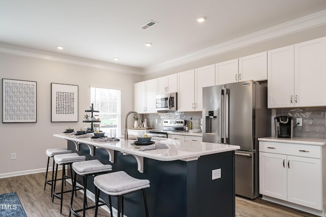 kitchen with white cabinetry, appliances with stainless steel finishes, a kitchen island with sink, and decorative backsplash