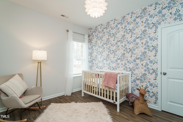 bedroom featuring an inviting chandelier, dark wood-type flooring, and a crib