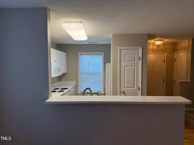 kitchen with kitchen peninsula, a textured ceiling, and white appliances