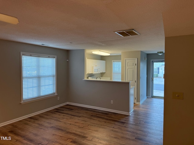 empty room featuring a healthy amount of sunlight, dark wood-type flooring, and a textured ceiling