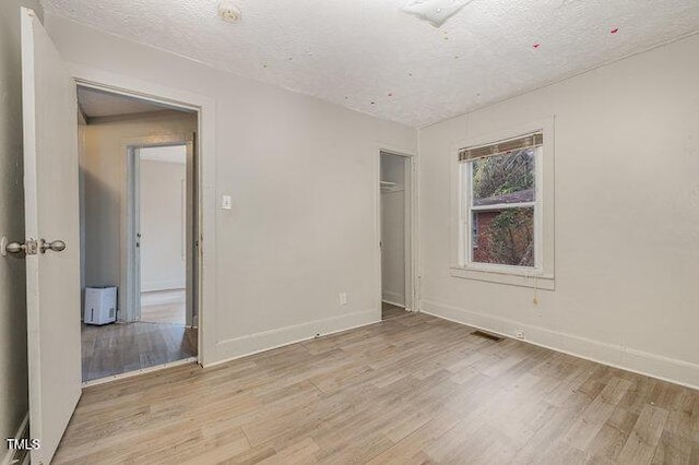 unfurnished bedroom with light wood-type flooring, a textured ceiling, and a closet