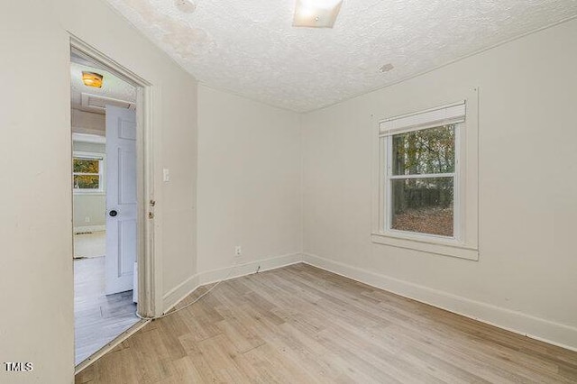 spare room featuring a textured ceiling, a wealth of natural light, and light hardwood / wood-style flooring