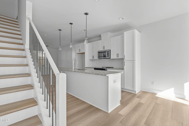 kitchen featuring white cabinetry, light stone counters, a kitchen island with sink, stainless steel appliances, and light hardwood / wood-style floors