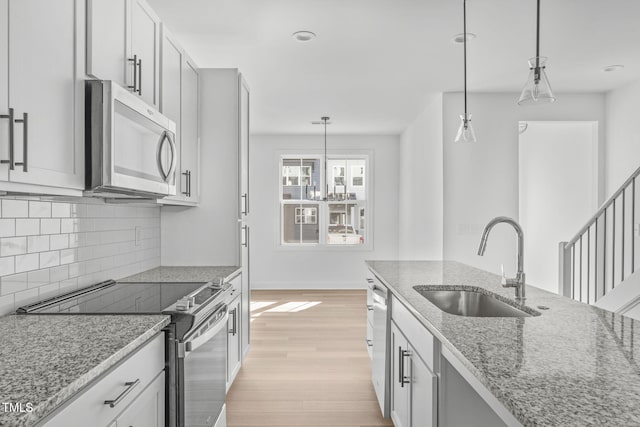 kitchen with sink, hanging light fixtures, light hardwood / wood-style flooring, appliances with stainless steel finishes, and light stone countertops